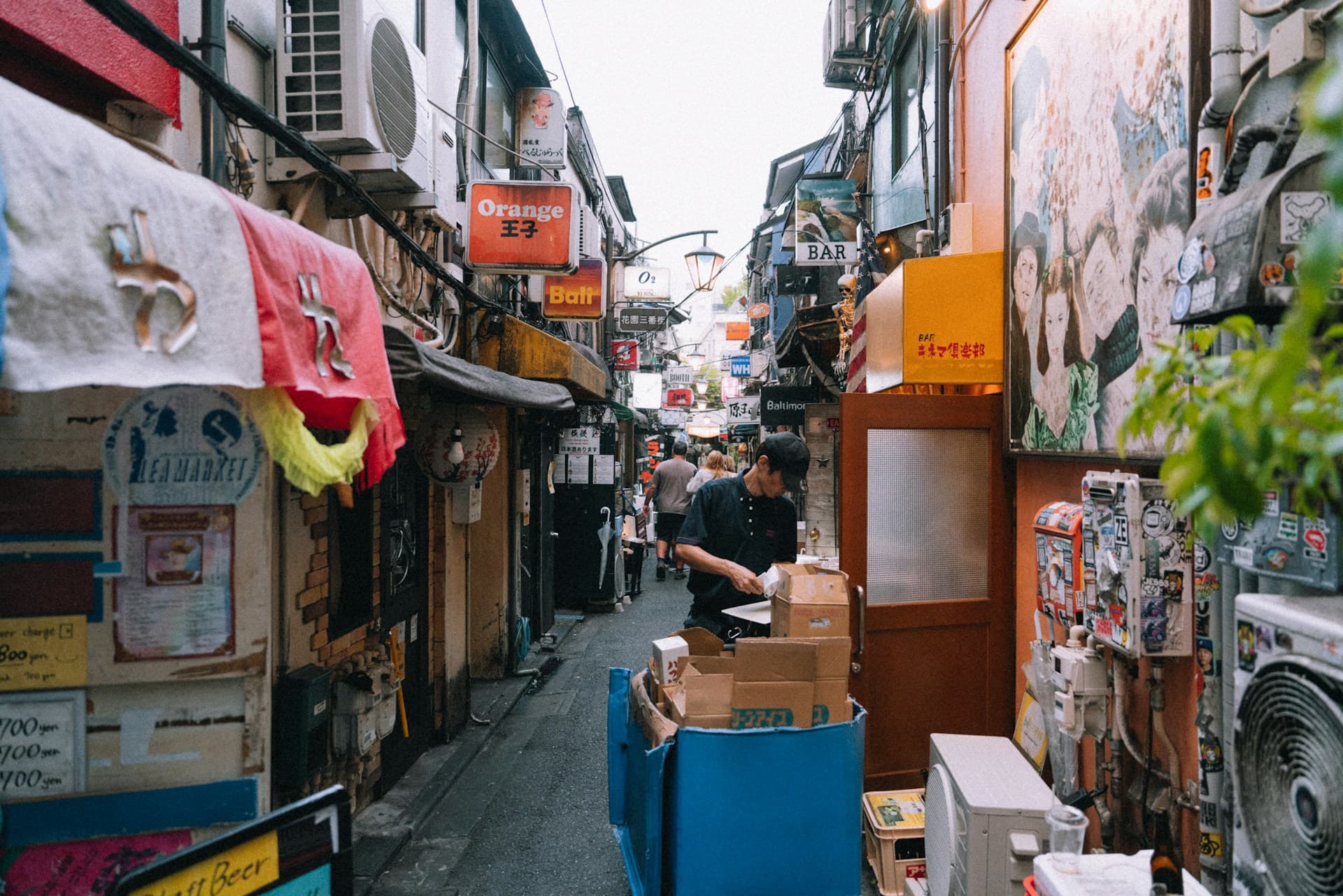 Dense alley scene with signs, storefronts, and a foreground worker