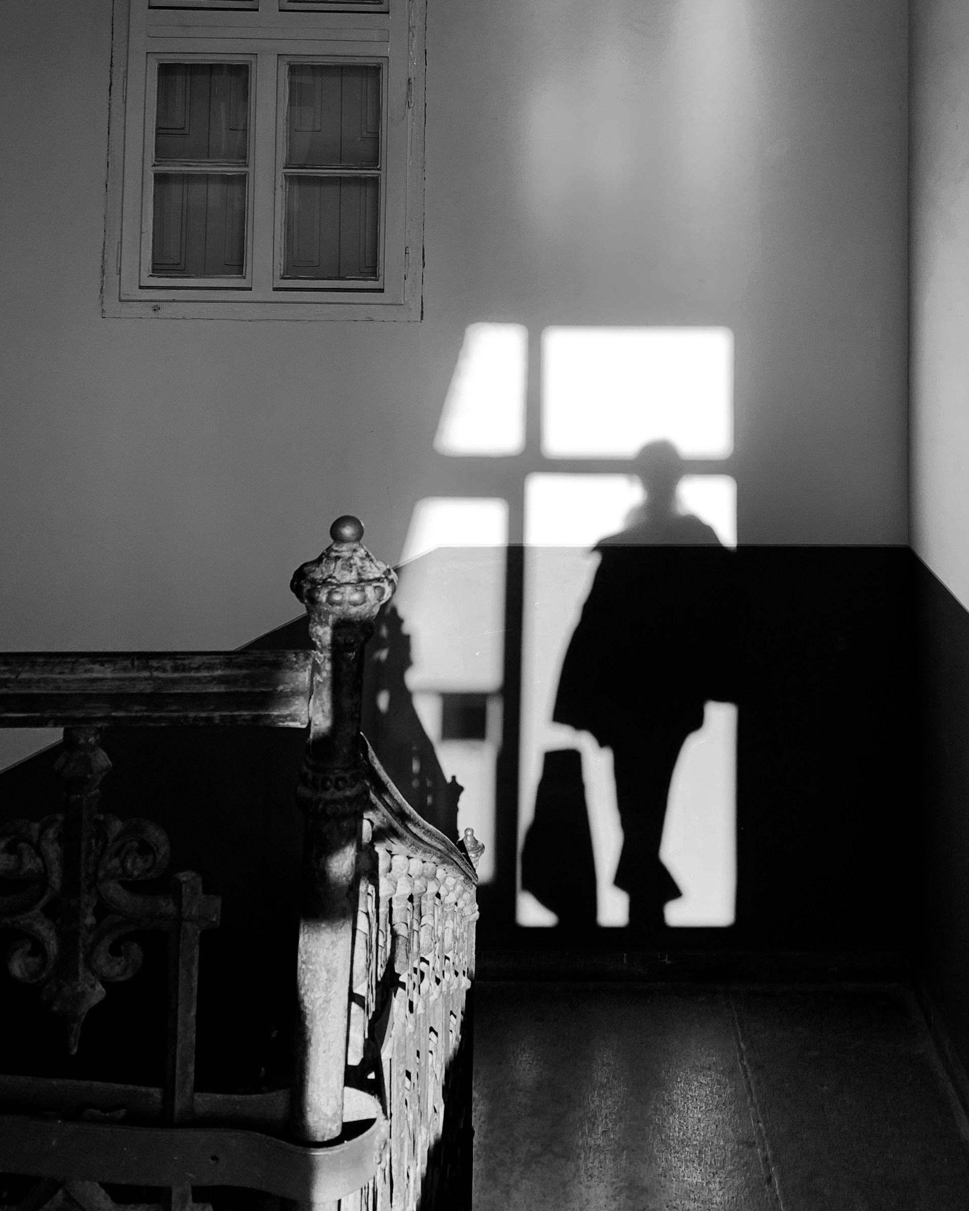 Black and white study of a human shadow framed by hard window light