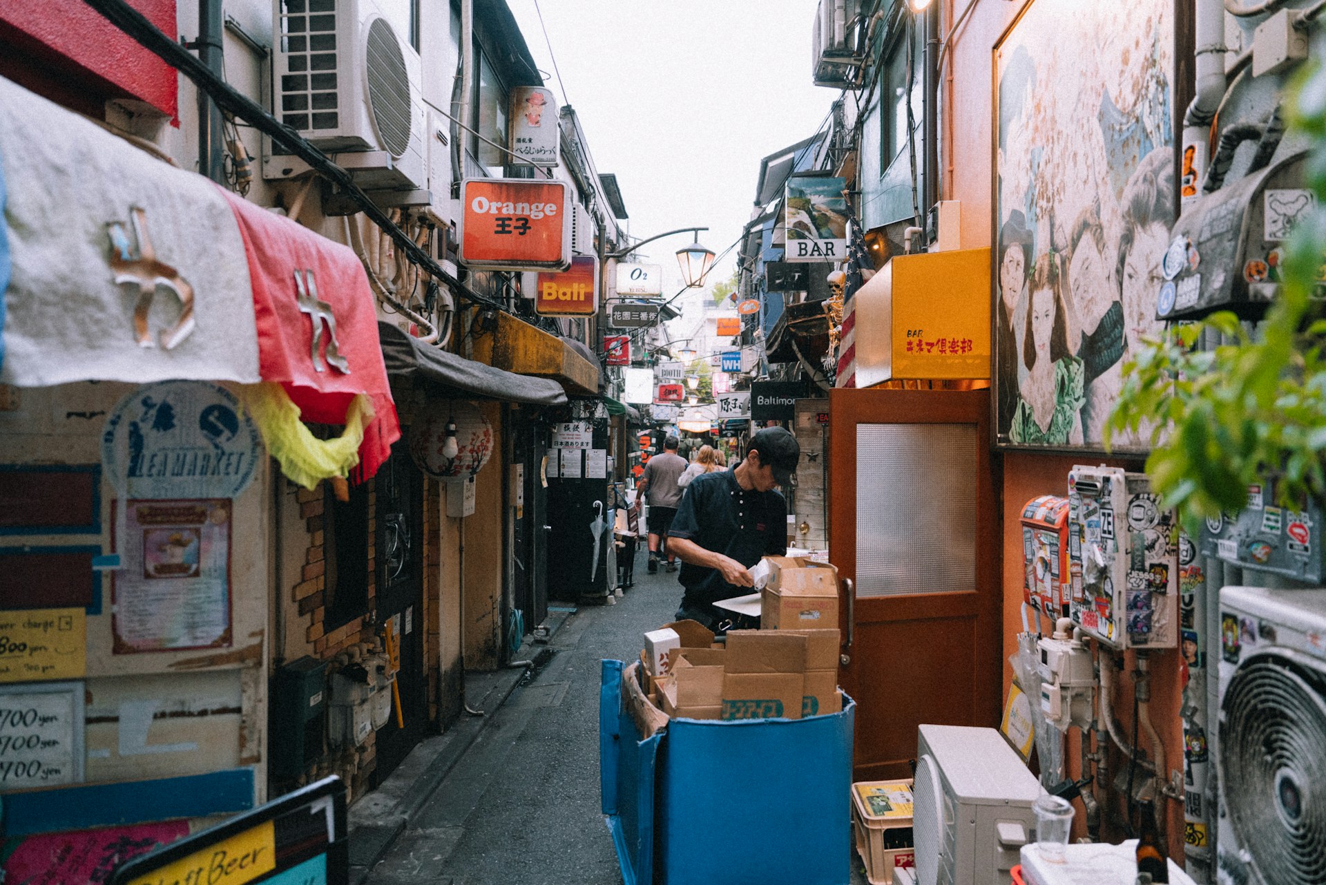 Dense alley scene with signs, storefronts, and a foreground worker